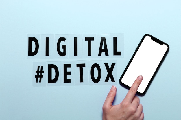 Phrase Digital detox and female hand with smarthone. Blue background,hashtag, top view.