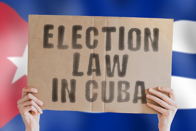 The phrase Election law in Cuba on a banner in men's hands with a blurred Cuban flag in the background Constitution Political Senate Havana Electorate Majority