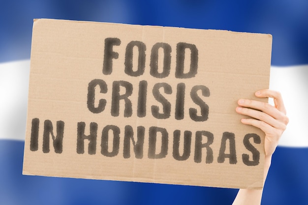 The phrase Food crisis in Honduras is on a banner in men's hands with a blurred background Crisis Finance Life Nutrition Bread Disaster Collapse Social issue Problem