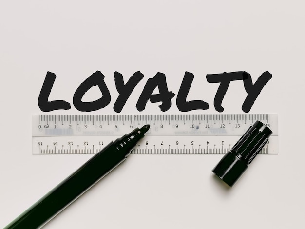 Phrase LOYALTY written on white background with plastic ruler and marker pen.