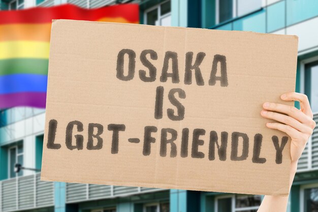 男性の手のバナーに「大阪はLGBTフレンドリー」というフレーズがあり、背景にLGBTの旗がぼやけています。人間関係。違う。多様。自由。セクシュアリティ。社会問題。社会