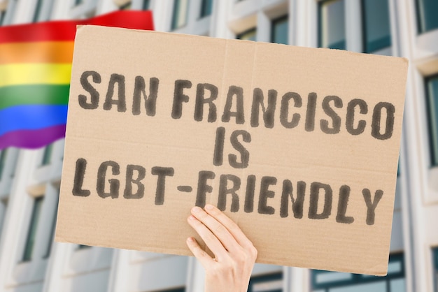 "San Francisco is LGBT-Friendly"라는 문구가 배경에 흐릿한 LGBT 깃발이 있는 남성의 손에 있는 배너에 있습니다. 인간 관계. 다른. 다양한. 자유. 성별. 사회 문제. 사회