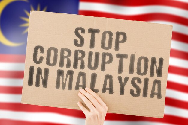 말레이시아의 부패 중지라는 문구는 배경에 흐릿한 말레이시아 국기가 있는 남성의 손에 있는 배너에 금지된 부범죄 부패 경제 부패 가능한 정치를 방지합니다.