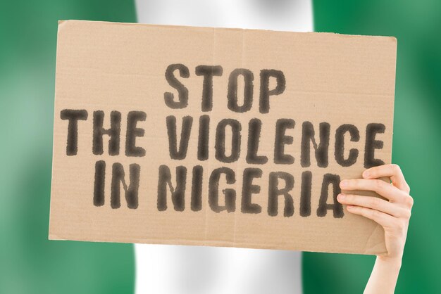 The phrase stop the violence in nigeria is on a banner in men\'s\
hands with a blurred nigerian flag in the background sad rights\
security social stress combat hate cruelty furious hitting