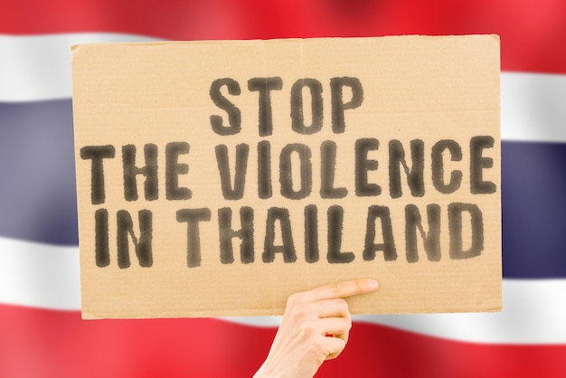 The phrase stop the violence in thailand is on a banner in\
men\'s hands with a blurred thai flag in the background sad rights\
security social stress combat hate cruelty furious