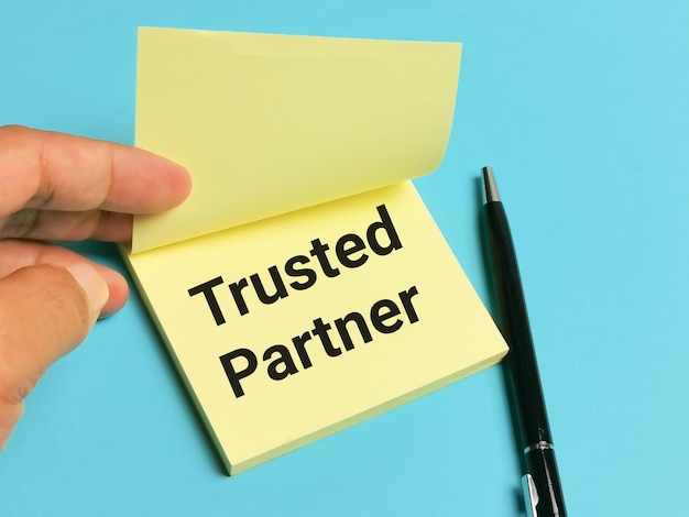 Phrase trusted partner on sticky note with pen and hand.