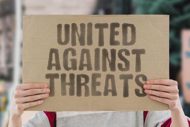 The phrase United against threats is drawn on a carton banner in men's hands Partnership Community Arm Safety Protection Action Armor Weapon Guard Defence Warning Risk Hazard