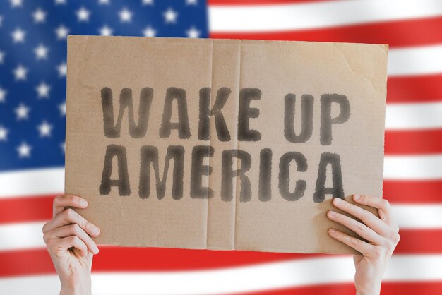 The phrase Wake up America on a banner in men's hand with blurred American flag on the background Government Protest Control Freedom Movement Power