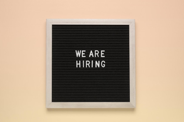 The phrase we are hiring on black letter board over isolated beige background