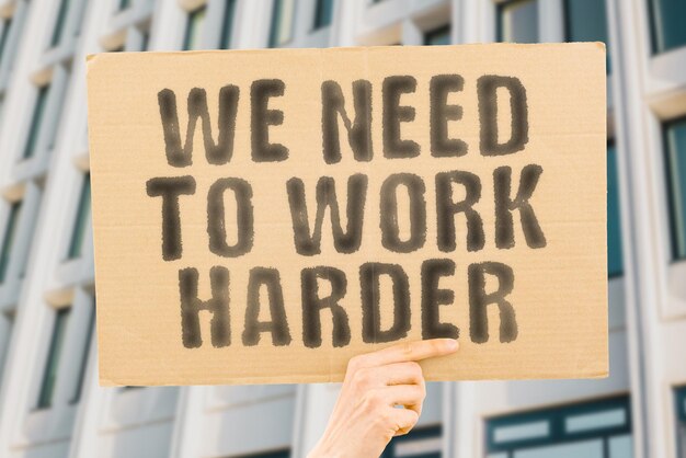 The phrase We need to work harder is on a banner in men's hands with blurred background Productivity Position Practice Employment Occupation Worker Working Strong Task Winner Productive