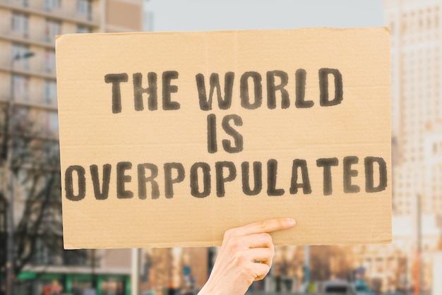 The world is overpopulated라는 문구는 흐릿한 배경 팀워크 시장 경제 글로벌 성장 작업 네트워크 직원 진행 자원 추세 도시가 있는 남성의 손에 있는 배너에 있습니다.