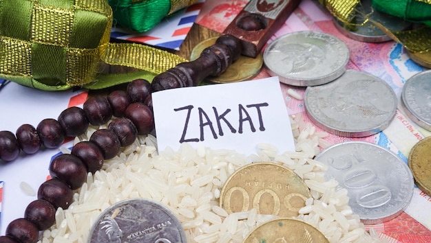 Phrase ZAKAT written on white tag with rice rosary beads and coins Selective focus