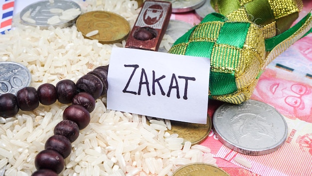 쌀 묵주와 동전이 있는 흰색 태그에 쓰여진 문구 ZAKAT 선택적 초점