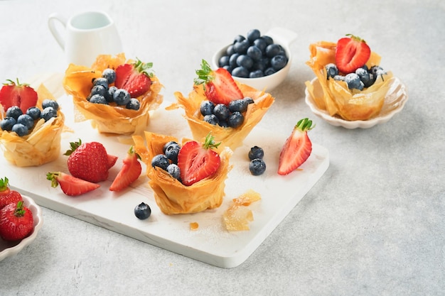 Phyllo or filo pies with fresh berries strawberries and blueberries cheese filling topped with fresh mint on white plate homemade filo pastry paskets delicious filo pastry dessert