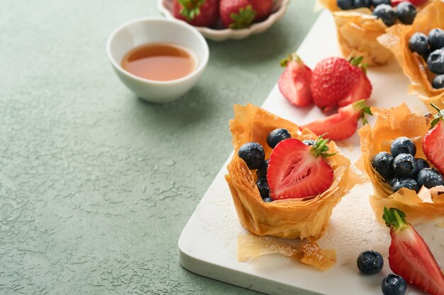 Phyllo or filo pies with fresh berries strawberries and blueberries cheese filling topped with fresh mint on white plate Homemade Filo pastry paskets Delicious filo pastry dessert