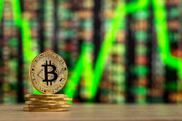 Bitcoin fisico in piedi a un tavolo di legno davanti a un grafico di numeri