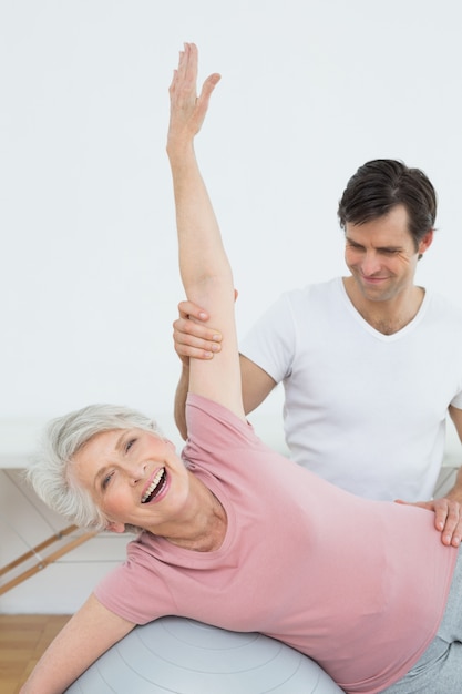 Foto fisioterapista che assiste la donna senior con la palla di yoga