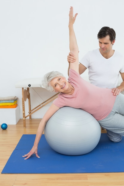 Physical therapist assisting senior woman with yoga ball