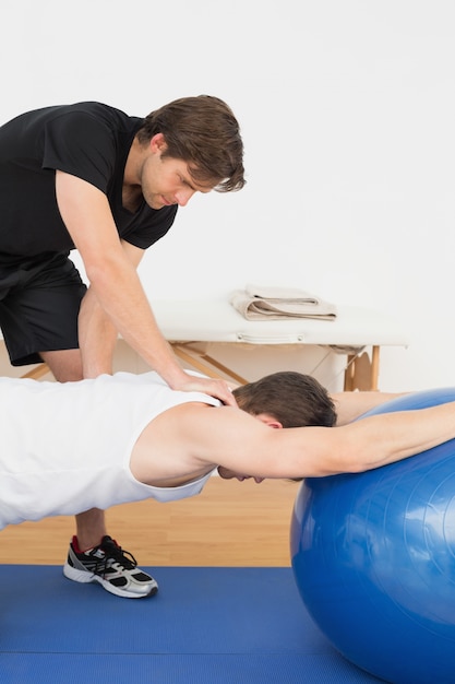 Physical therapist assisting young man with yoga ball