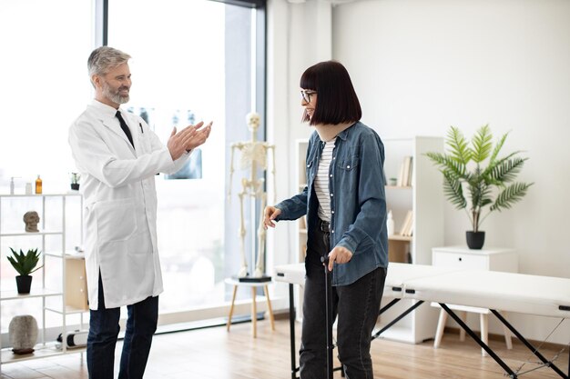 Photo physician applauding lady on standing without aid using cane