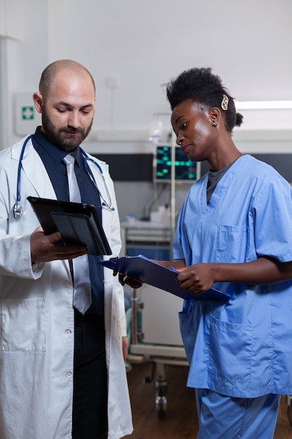 Physician doctor with afro american assistant monitoring recovery treatment using tablet computer working in hospital ward