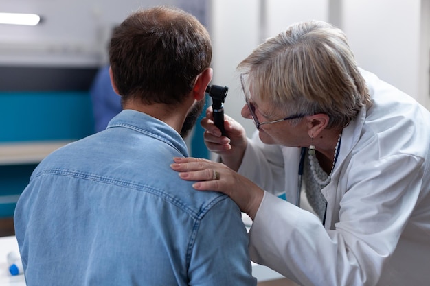 Medico che fa l'esame dell'orecchio con l'otoscopio per il paziente in ufficio. medico di medicina generale che tiene in mano uno strumento medico per consultare un uomo durante la visita di controllo. test di otorinolaringoiatria