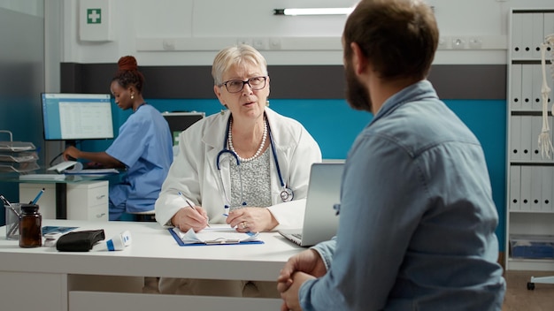 Physician and man having conversation about health care at\
appointment, doing checkup examination visit. giving prescription\
medicine and treatment to patient with illness in medical\
office.