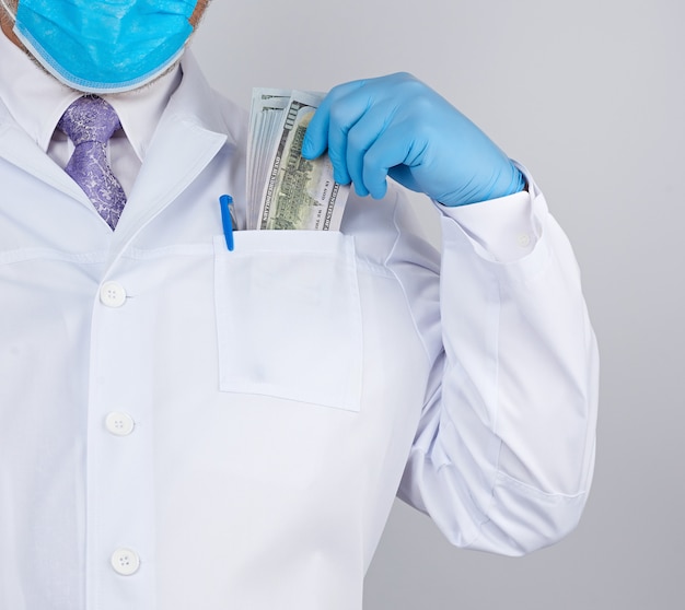 白衣を着た医師、青い滅菌手袋を着用、医師が紙幣のパックを保持