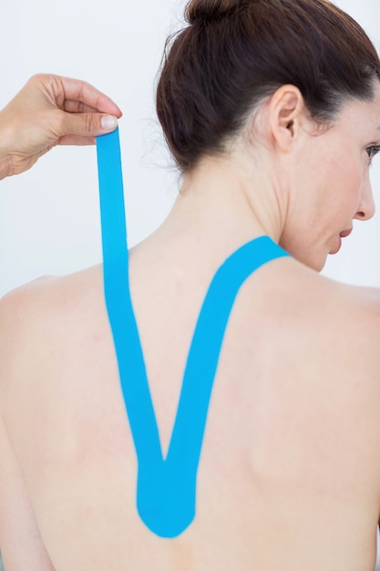 Physiotherapist applying blue kinesio tape to patients back 