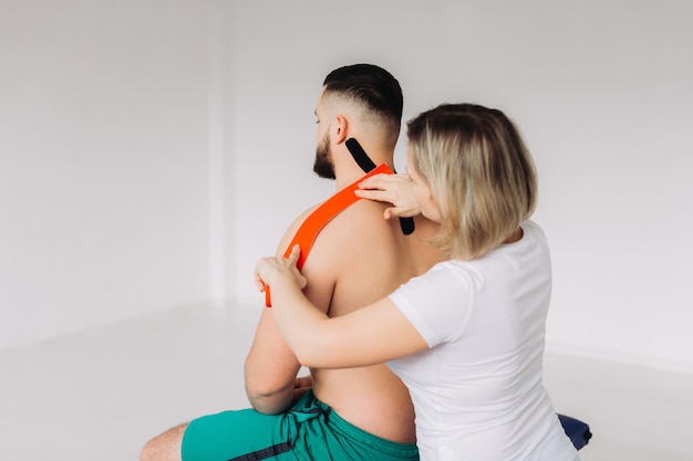 Physiotherapist applying red and black kinesio tapes to patients back in his office.