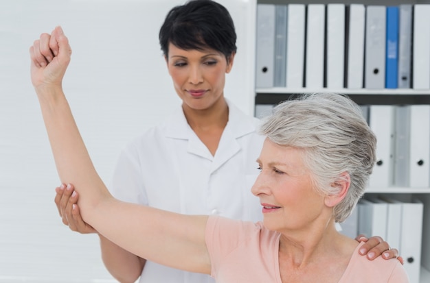 Physiotherapist assisting senior woman to stretch her hand