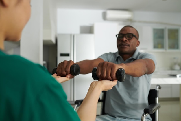 Photo physiotherapist controlling patient lifting dumbbells to train muscles