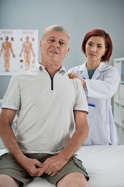 Физиотерапевт осматривает пожилого пациента, она массирует различные триггерные точки на его спине и спрашивает, больно ли это.