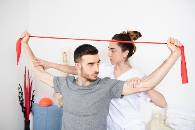 Physiotherapist helping to an athletic man to make rehabilitation exercises with a pilates rubber band.