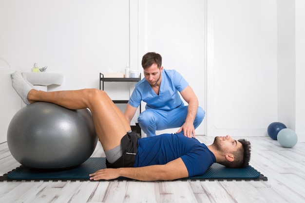 Physiotherapist helps handsome young patient with pilates exercises