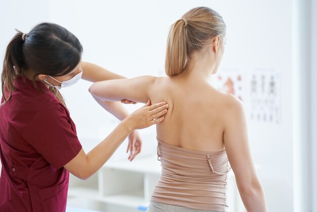 physiotherapist in mask helping female patient