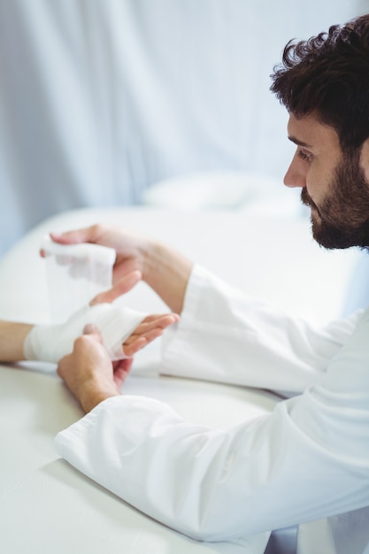 Physiotherapist putting bandage on injured hand of patient