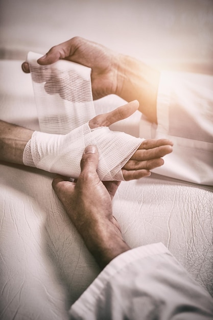 Physiotherapist putting bandage on injured hand of patient