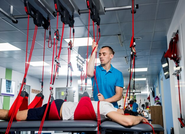 Physiotherapy. Suspension training therapy. Young man doing fitness traction