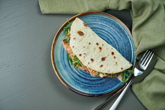 Piadina - classic Italian tortilla-bread with prosciutto, arugula, mozzarella and tomatoes on a blue plate on wooden table. Fast sandwich. Top view, flat lay with copy space