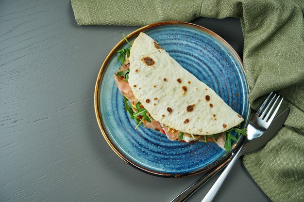 Piadina - klassiek italiaans tortilla-brood met ham, rucola, mozzarella en tomaten op een blauw bord op houten tafel. snelle sandwich. bovenaanzicht, plat lag met kopie ruimte