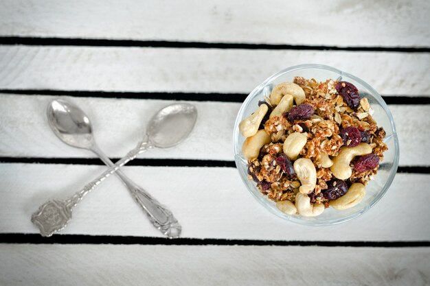 Piala met granola en twee gekruiste lepels op een witte houten doos. detailopname