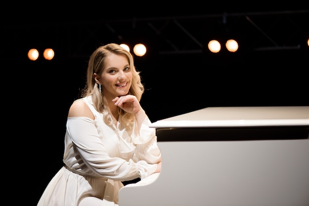 Foto pianista in posa vicino al pianoforte bianco sul palco