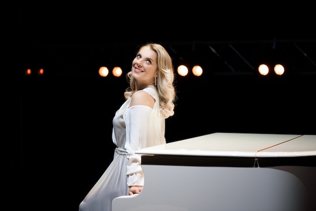 Pianist posing near white piano on the stage