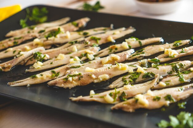 Pickled anchovies with garlic and parsley in a dark plate close-up.