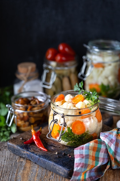 Pickled cauliflower with carrots in a glass jar on a dark wooden table.