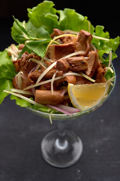 Pickled chanterelle mushrooms, with herbs and lettuce, in a glass bowl, on a black background