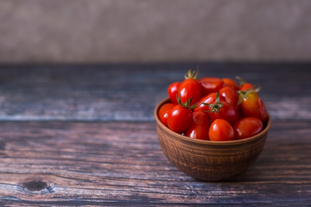 Pickled cherry tomatoes in clay plate on wooden background