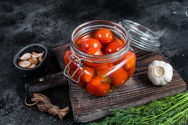 Pickled cherry tomatoes in a glass jar with herbs