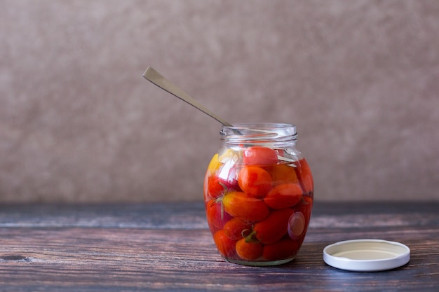 Pickled cherry tomatoes in glass jar on wooden background